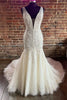 Robe de mariée longue blanche en tulle et dentelle, coupe sirène, décolleté plongeant en V, traîne brossante